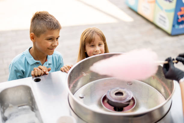 Little girl and boy waiting for a sweet cotton candy at amusement park Little girl and boy waiting for a sweet cotton candy to be made at the counter shop while visiting amusement park during a summer vacation child cotton candy stock pictures, royalty-free photos & images