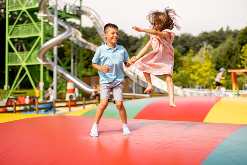 Kids jumping on inflatable trampoline, having fun visiting amusement park during a summer vacation. Brother with a sister spending leisure time together