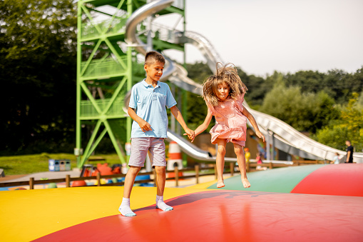 Kids jumping on inflatable trampoline, having fun visiting amusement park during a summer vacation. Brother with a sister spending leisure time together
