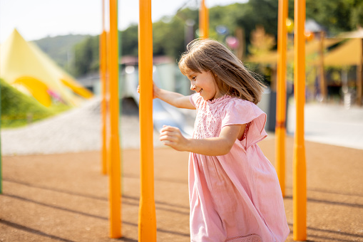 Happy little girl playing on a children's playground during a summertime. Concept of childhood and entertainment