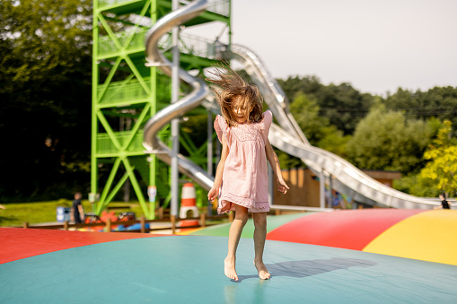 Little girl jumping on inflatable trampoline, having fun visiting amusement park during a summer vacation