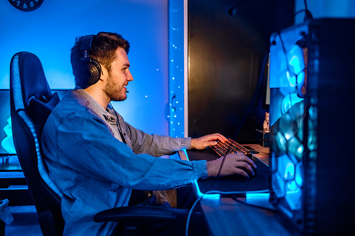 Young gamer enjoying playing games at home on his desktop PC at night having beautiful lights around.