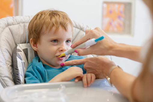 Feeding specialist holding designed spoon and stimulating blond toddler's mouth in feeding therapy, oral motor skills, occupational therapy