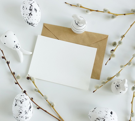 Card mockup, envelope ,Easter eggs and funny bunny decor ,spring willow branches in neutral colors on white background top view flatlay. Copy space.Easter background.