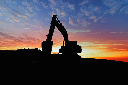 Silhouette of excavator bucket in the construction site with cityscape background at sunset time