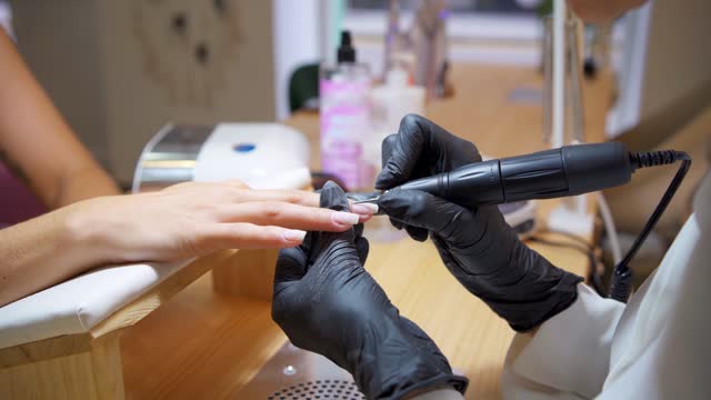Close-up video of a technician shaping the nails of a client with an electric file
