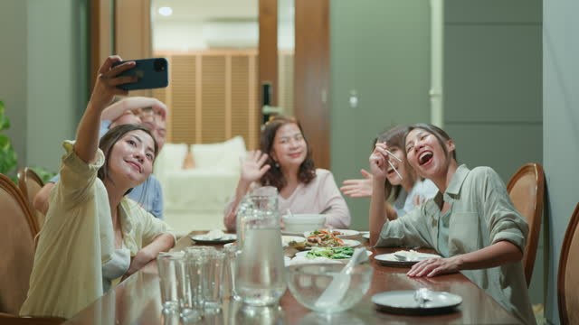 Asian multi-generation family reunion taking selfies photo at night while having a conversation and sharing stories at the dinner table in the front yard.