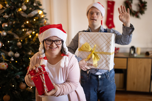 Portrait of a Caucasian man and woman with Down syndrome holding Christmas presents in the living room of a house