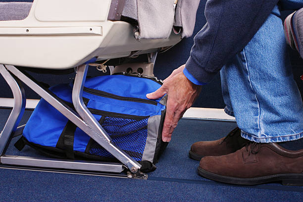 Carry-on Luggage Airplane passenger stowing his carry-on luggage under the seat in front of him. gchutka stock pictures, royalty-free photos & images