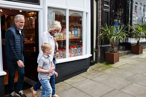 Man, woman and kid on street by candy shop for ice cream, shopping and choice for love, care or bonding. Grandparents, boy child and retail store with walk for sweets, ice pop or dessert with family