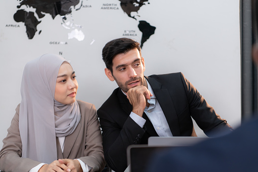 In a modern office, a hijab businesswoman and a businessman talking and use a smart phone while in a meeting.