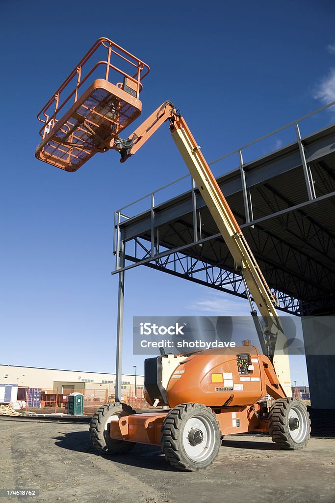 Human Lift An orange human lift sitting outide a newly constructed building Scissor Lift Stock Photo
