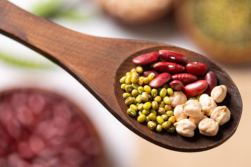 Top view of a wooden spoon full of various raw legumes such as chickpeas, green soybeans and kidney beans