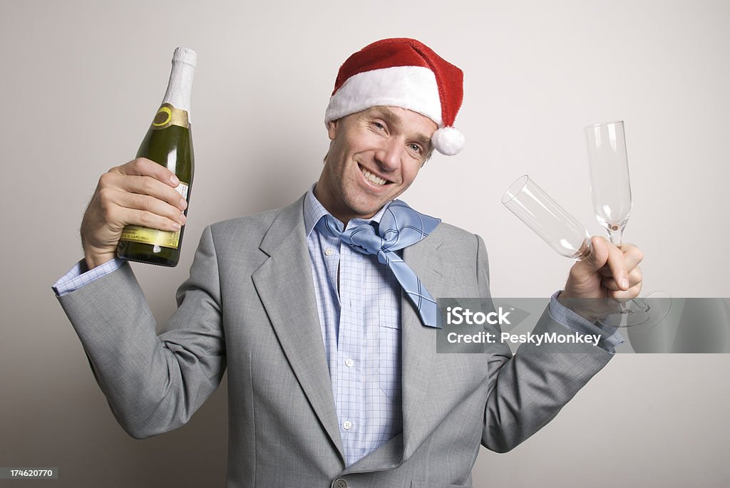 Office Worker Businessman Toasts at Holiday Party Businessman in Santa hat looks a little sloppy holding a bottle of champagne and two glasses looking at the camera Bottle Stock Photo