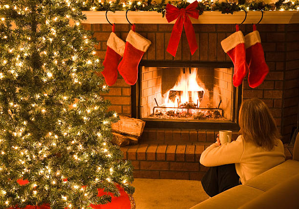 istock woman sitting by Christmas tree and blazing fire in fireplace 174621107