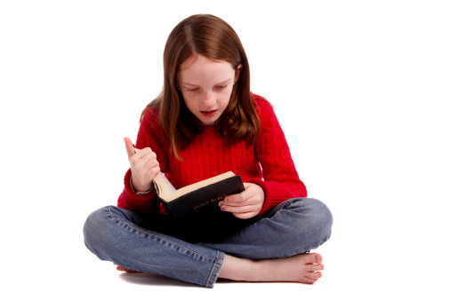 Little girl sitting cross legged and reading the Bible