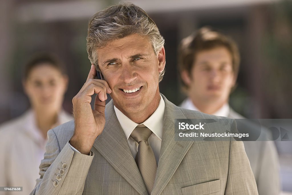 Smiling mature businessman talking on cellphone Closeup of a smiling mature businessman talking on cellphone with colleagues in the background 50-54 Years Stock Photo