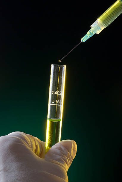 Bottles with vaccine in the background and selective focus on a needle with a drop of a medicine. Preparation for injecting the medicine and vaccination. White background. Studio shot
