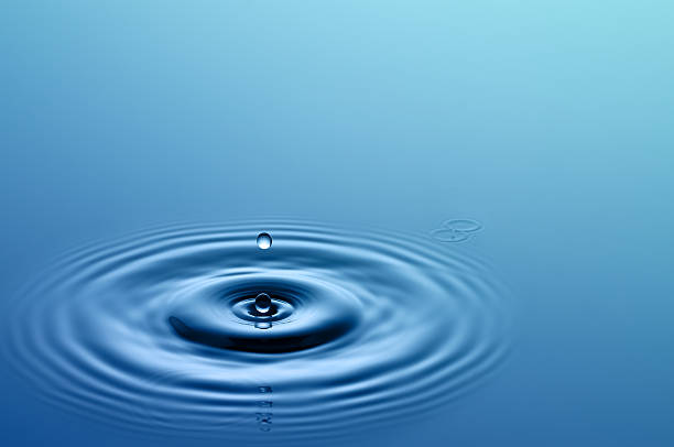 Single drop of water hitting a larger body of water stock photo