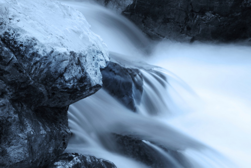 Long time exposure of flowing water around rocks. Monochrome blue