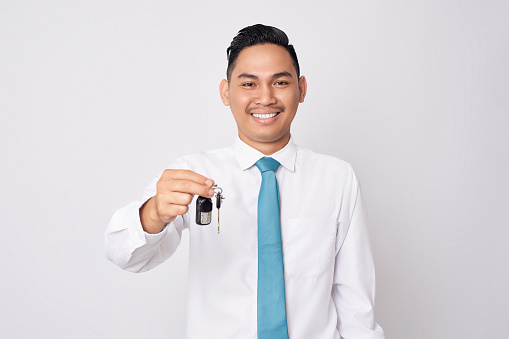 Smiling happy young Asian businessman holding car key in hand isolated on white background. Achievement career wealth business concept