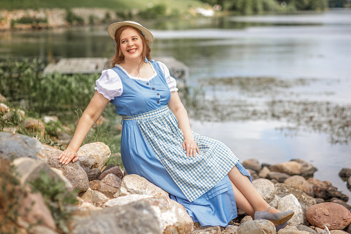A beautiful retro woman in a blue dress and hat outdoors on the riverbank