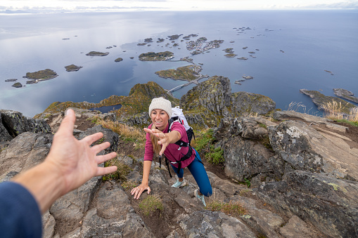 Two hikers helping each other to reach top of rock, Autumn, Norway