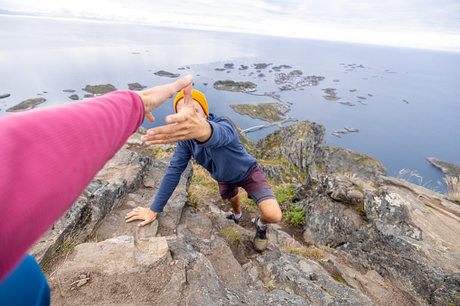 Two hikers helping each other to reach top of rock, Autumn, Norway