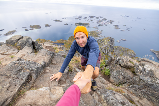 Two hikers helping each other to reach top of rock, Autumn, Norway