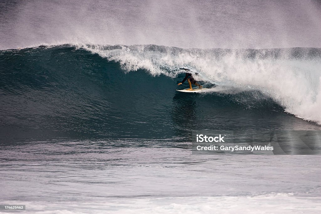 Surfing In The Curl of a big wave A Maui surfer crouching on his board in the curl of a big wave on Maui's north shore. Activity Stock Photo