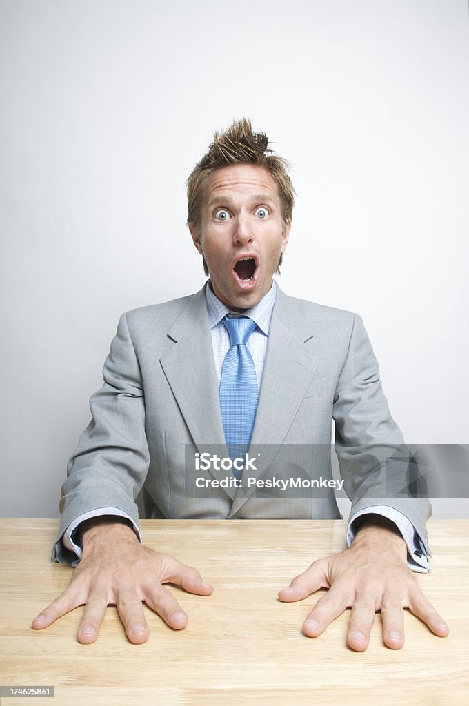 Hands-Down Surprise Businessman Sitting at Desk Wide Eyes Office worker slaps his hands on the desk with a look of open-mouth shock Bad News Stock Photo