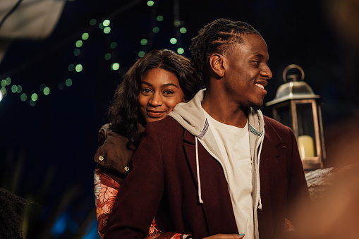 A couple standing outdoors together at nighttime in Northumberland, North East England. The woman has her arms around her boyfriend while she looks at the camera and smiles.\n\nVideos also available for this scenario.