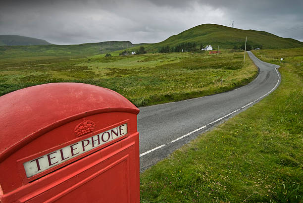 Red telephone booth in a narrow road on north of Isle of Skye. Upper view of the phone box, the road and the green fields.