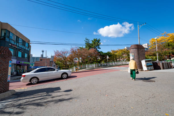 Cheonan, South Korea - October 20, 2023: That all cities in Korea are rapidly aging is the biggest social problem in Korea. It is difficult to see young children in suburban cities. An elderly woman walking down a road with a cloud floating around. (Photo by Young Jin Lee)