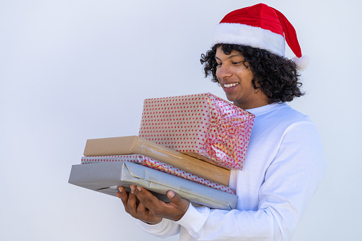 young hispanic man in Santa Claus hat carrying Christmas presents