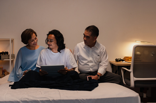 Young man talking to parents in bedroom with laptop.