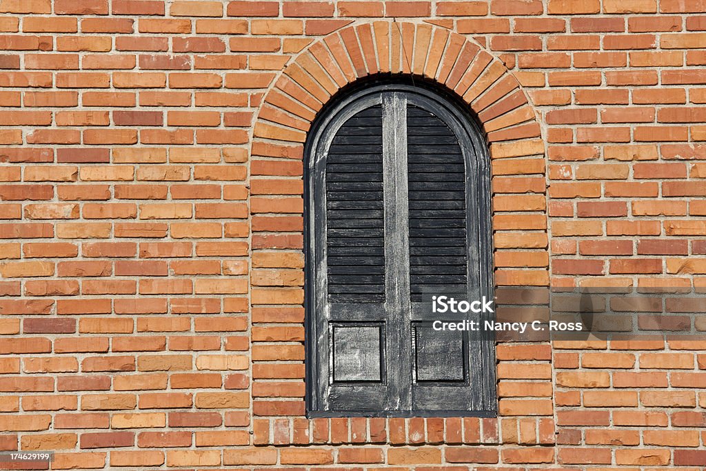 Arched Window on Bright Red Brick Wall, Building Exterior, Architectural "Shuttered, arched black window inset into red brick wall. Late afternoon sun." Arch - Architectural Feature Stock Photo