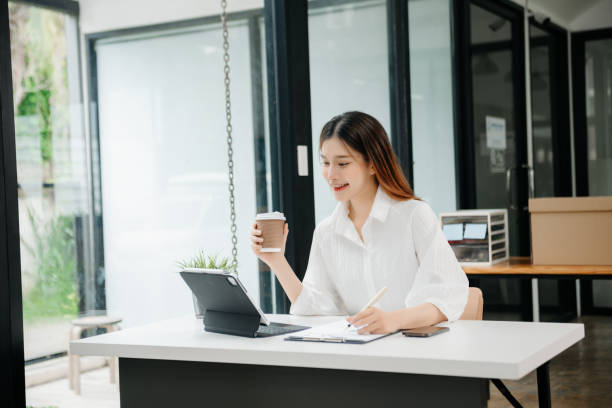 istock Young beautiful woman typing on tablet and laptop while sitting at the working white table modern office 1746293783