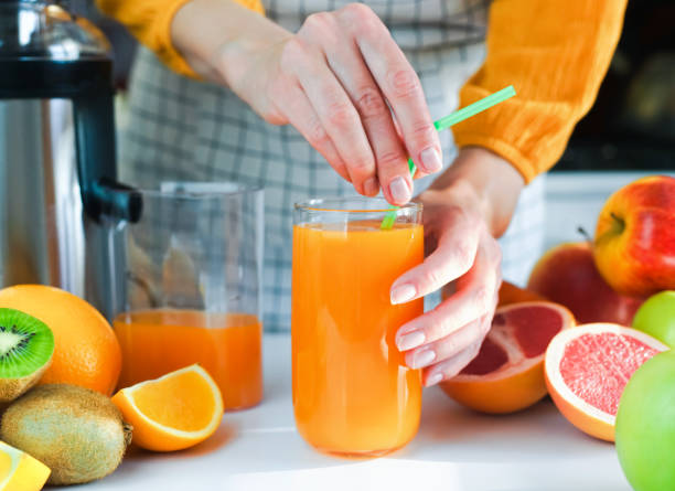 istock Woman's hands insert a straw into a glass with freshly squeezed fruit juice. A variety of fruits and a juicer on the table in the kitchen. Close-up. Selective focus. 1746295748