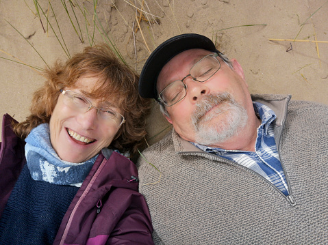 Mature woman takes a fun selfie of herself and her partner who is sleeping on the beach.