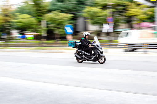 Cheonan City, South Korea - October 4, 2023: Demand for delivery has surged in the aftermath of COVID-19. The number of people working as delivery workers has also increased in South Korea. Delivery workers are often seen driving motorcycles while looking at their smartphones, which has become a social problem. A delivery man is riding a motorcycle while looking at his smartphone. (Photo by Young Jin Lee)