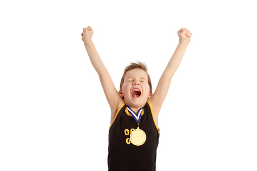 A young boy happily holds up his arms with a gold medal around his neck.
