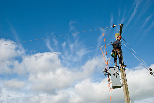 An unrecognisable utility workman carries out repairs on a transformer connected to an 11000 volt power line.