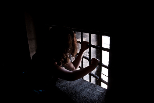 A girl trapped in a prison and looking through the prison bars.