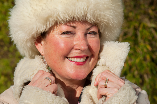 A happy, smiling senior female wearing a fur hat and jacket