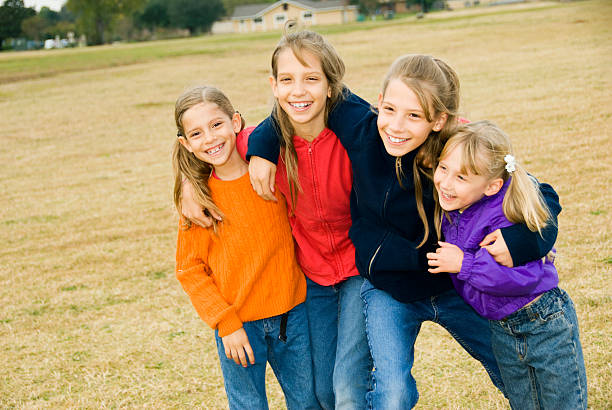 A group of children holding hands and playing in a bright, sunny park setting. The scene conveys clear feelings of happiness, friendship, and active enjoyment in the great outdoors.