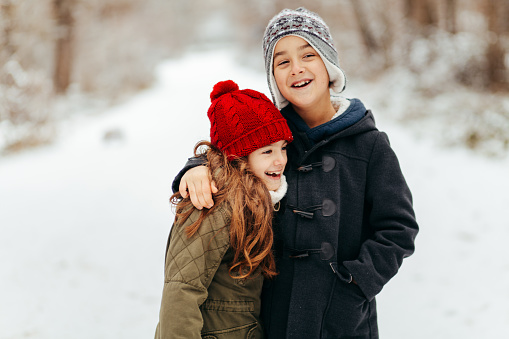 Children embrace and smiling while walking in the snowy forest and enjoys the snow in the winter