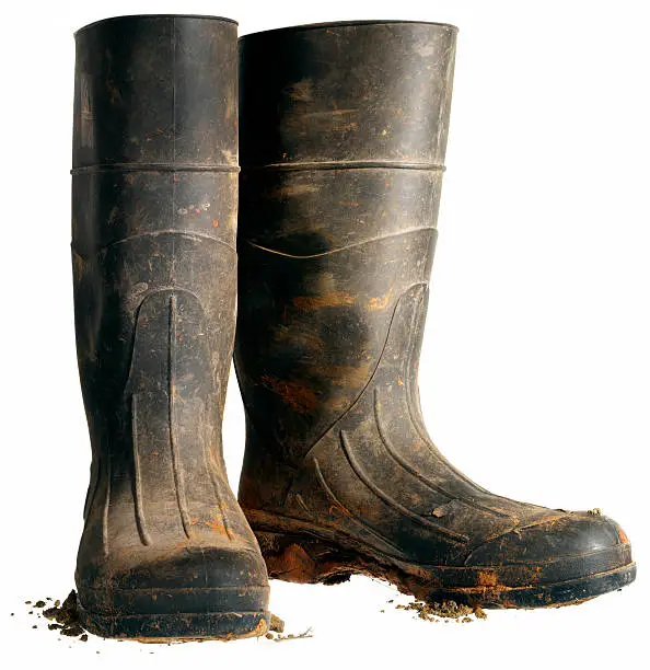 Hard working black rubber boots covered in dirt against a white background.
