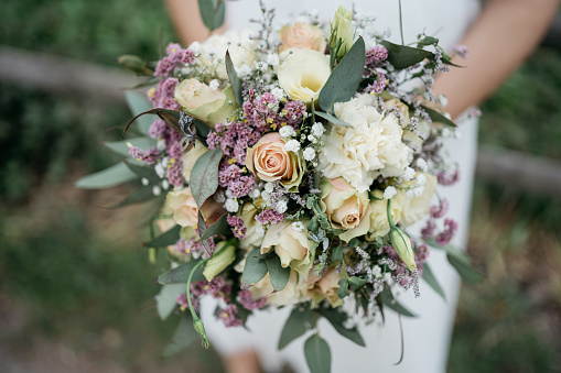 Bride holding b beautiful colorful wedding bouquet of roses, peonies and tulips in bright pink, coral and purple colors.