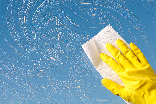 Hand in yellow protective glove is cleaning window, sky background stock photo
